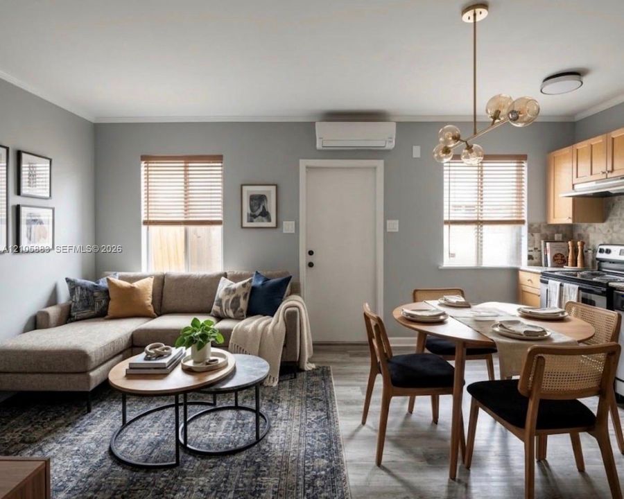 Open-concept area featuring light wood-finish flooring, a wall-mounted ductless mini-split system, multi-globe chandelier lighting, and kitchen cabinetry with wood-finish doors