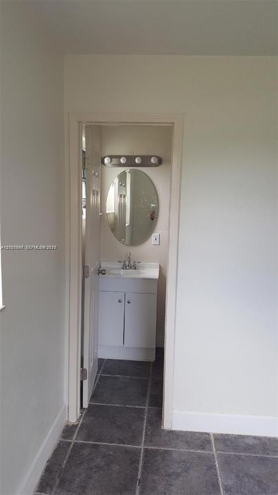 Bathroom featuring square tile flooring, a white vanity cabinet with an integrated basin, an oval wall-mounted mirror, and a four-bulb light fixture