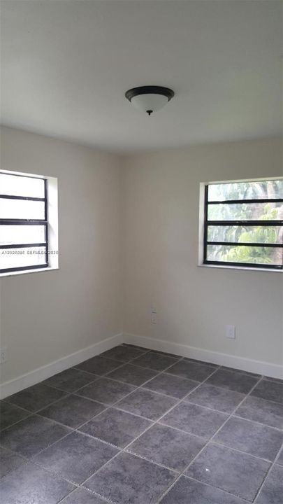 Neutral-toned interior featuring square stone-finish floor tiles, dual louvered windows, and a flush-mount dome light fixture