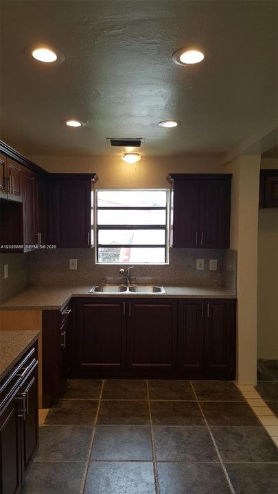 Dark wood cabinetry, speckled countertops, dual-basin stainless steel sink, large-format tile flooring, and recessed ceiling lighting