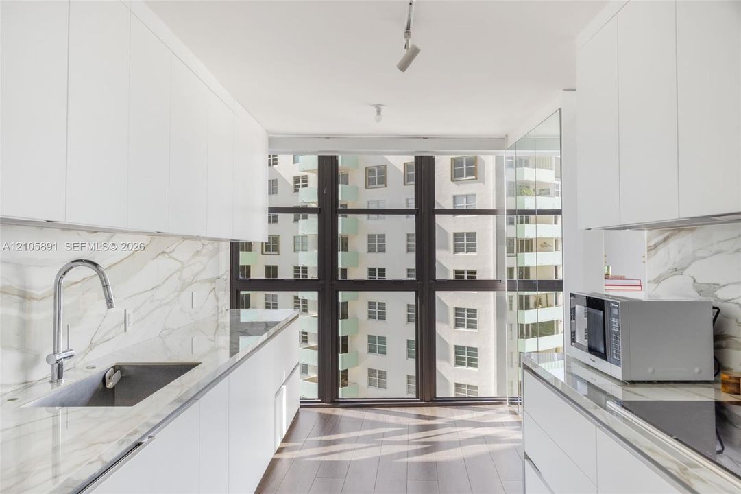 Kitchen featuring white flat-panel cabinetry, floor-to-ceiling windows, veined stone-finish countertops and backsplash, wood-finish flooring, and a stainless steel undermount sink with a gooseneck faucet