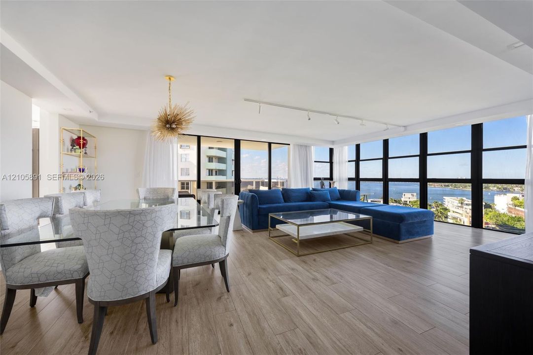 Open-concept living space featuring wood-finish flooring, floor-to-ceiling black-framed windows, and a decorative gold-finish pendant light