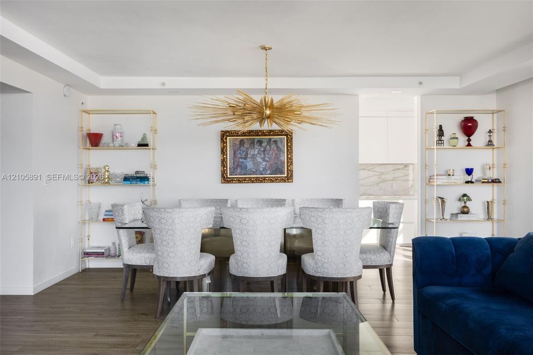 Dining area featuring wood-finish flooring, recessed ceiling detailing, two built-in gold-tone metal etagere shelves, and a prominent starburst chandelier