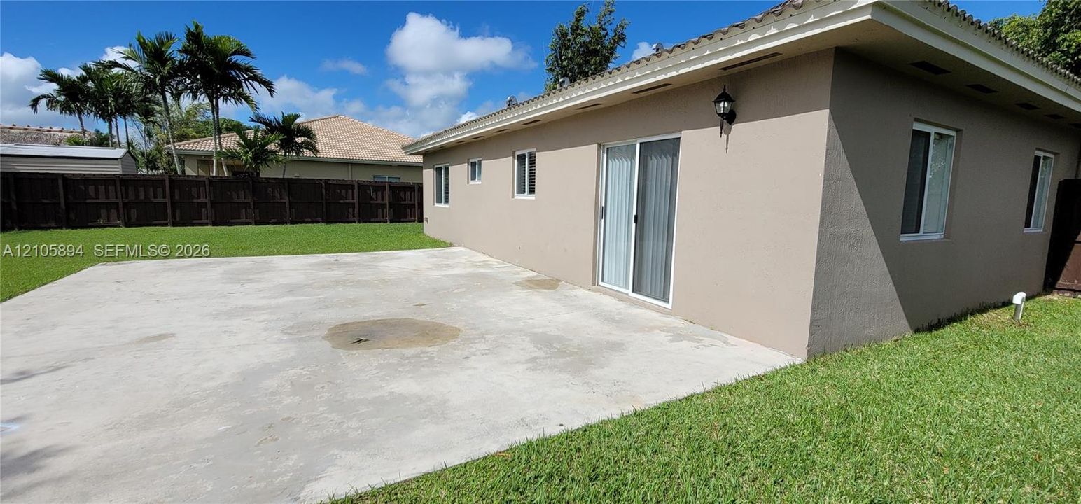 Stucco exterior featuring a concrete patio, sliding glass door, white-trimmed windows, and wood-panel perimeter fencing