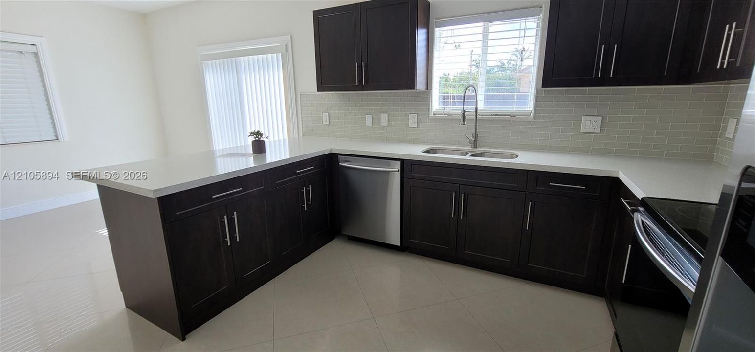 Kitchen featuring dark wood cabinetry, white countertops, stainless steel appliances, a light-toned tile backsplash, and tile flooring