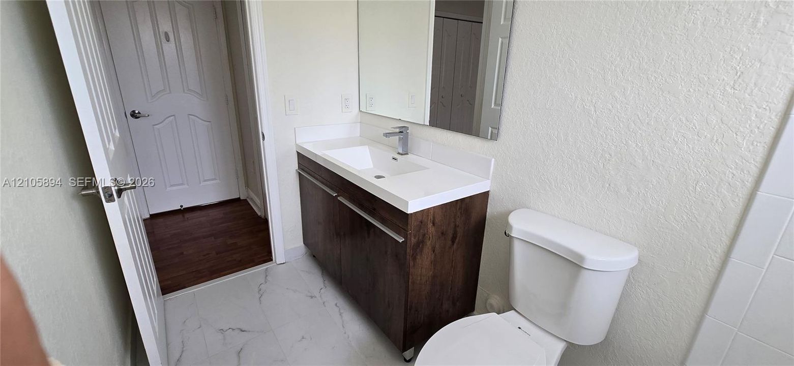 Bathroom vanity featuring a wood-finish cabinet, rectangular integrated basin, white solid-surface countertop, and single-handle faucet, complemented by large-format tile flooring