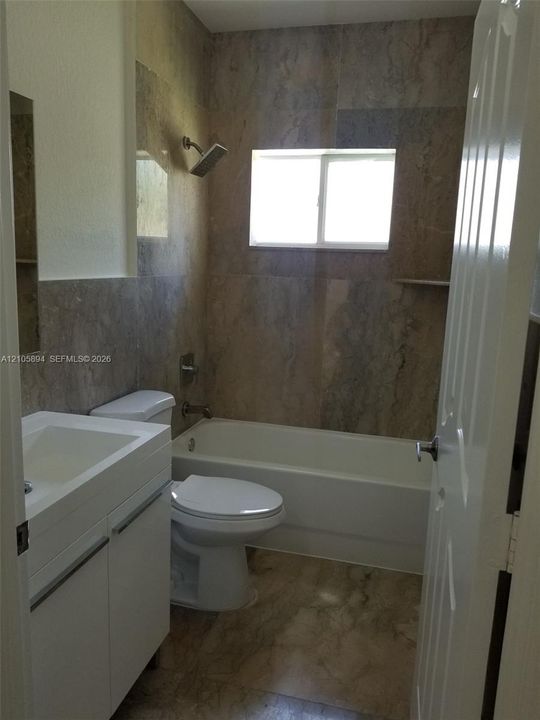 Full-height wall tile in the tub surround, white vanity cabinet with a rectangular basin, built-in shelving, and large-format floor tiling