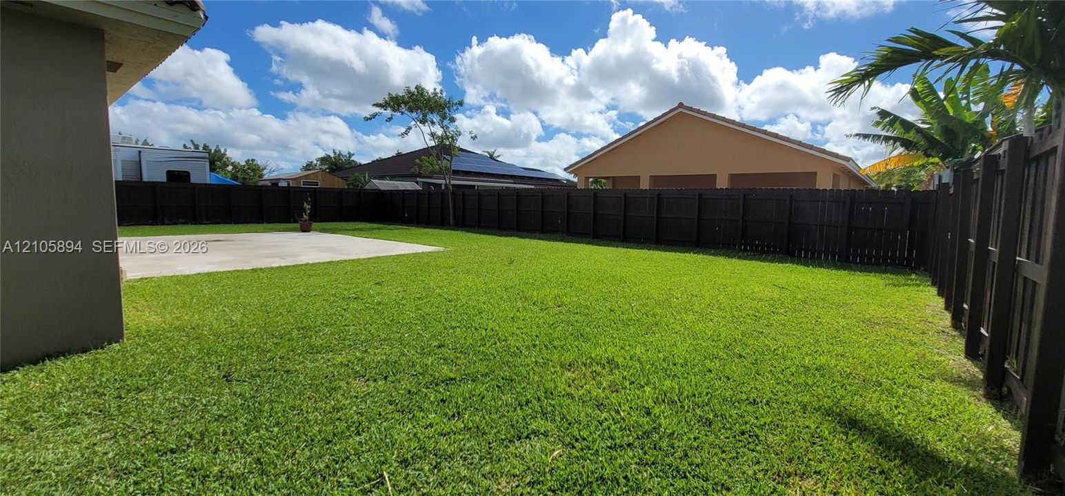 Backyard featuring a concrete patio, expansive lawn, and a perimeter wood privacy fence