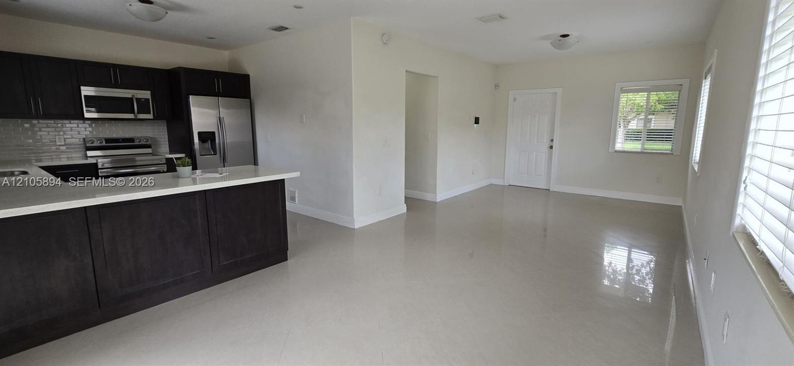 Kitchen featuring dark wood-finish cabinetry, a white countertop peninsula, a tiled backsplash, and stainless steel appliances, complemented by light-colored tile flooring throughout