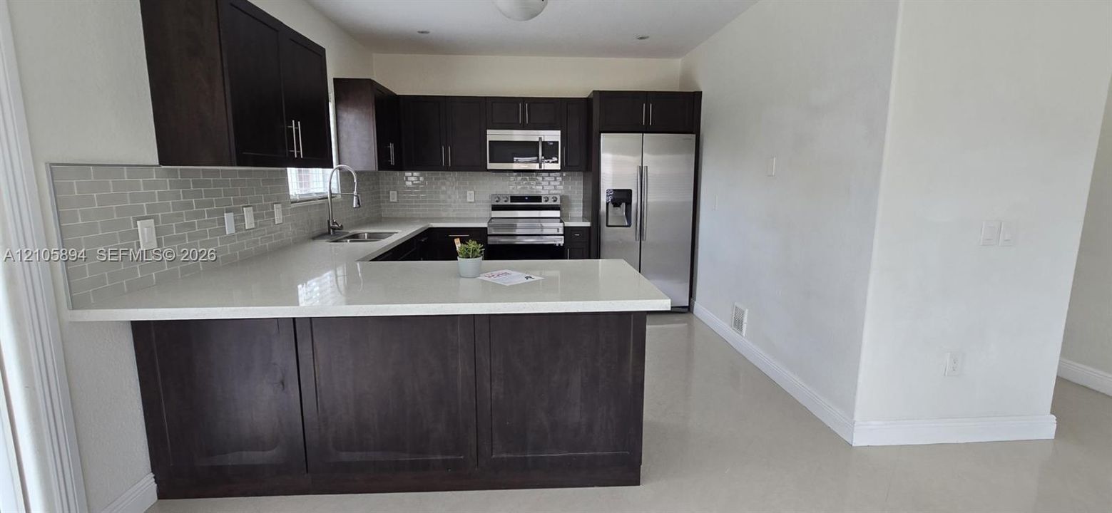 Kitchen featuring dark wood cabinetry, light-toned quartz countertops, a subway tile backsplash, and stainless steel appliances