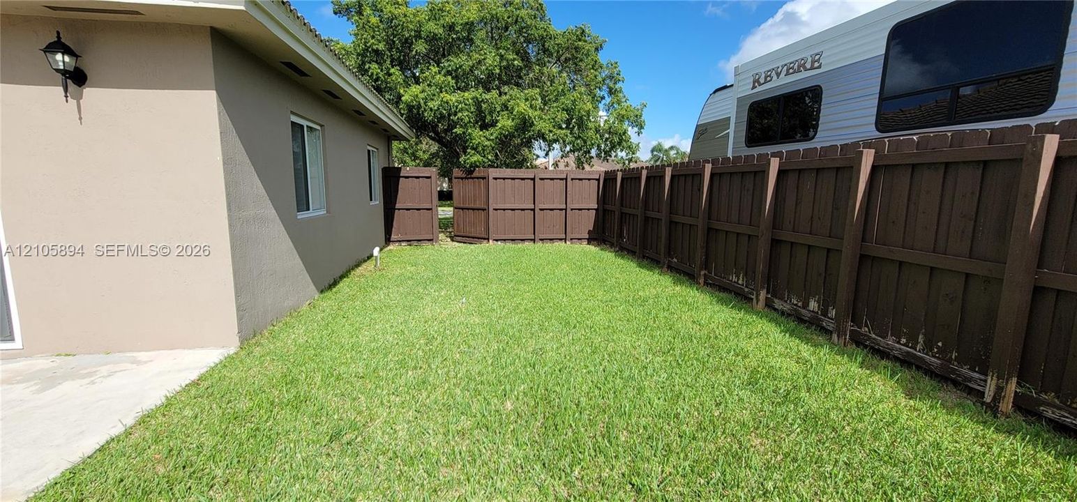 Side yard featuring a grass lawn, stained wood privacy fencing, and exterior wall-mounted lighting