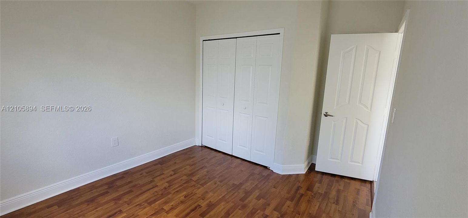 Neutral-toned interior featuring wood-finish flooring, white paneled closet doors, and a matching six-panel interior door