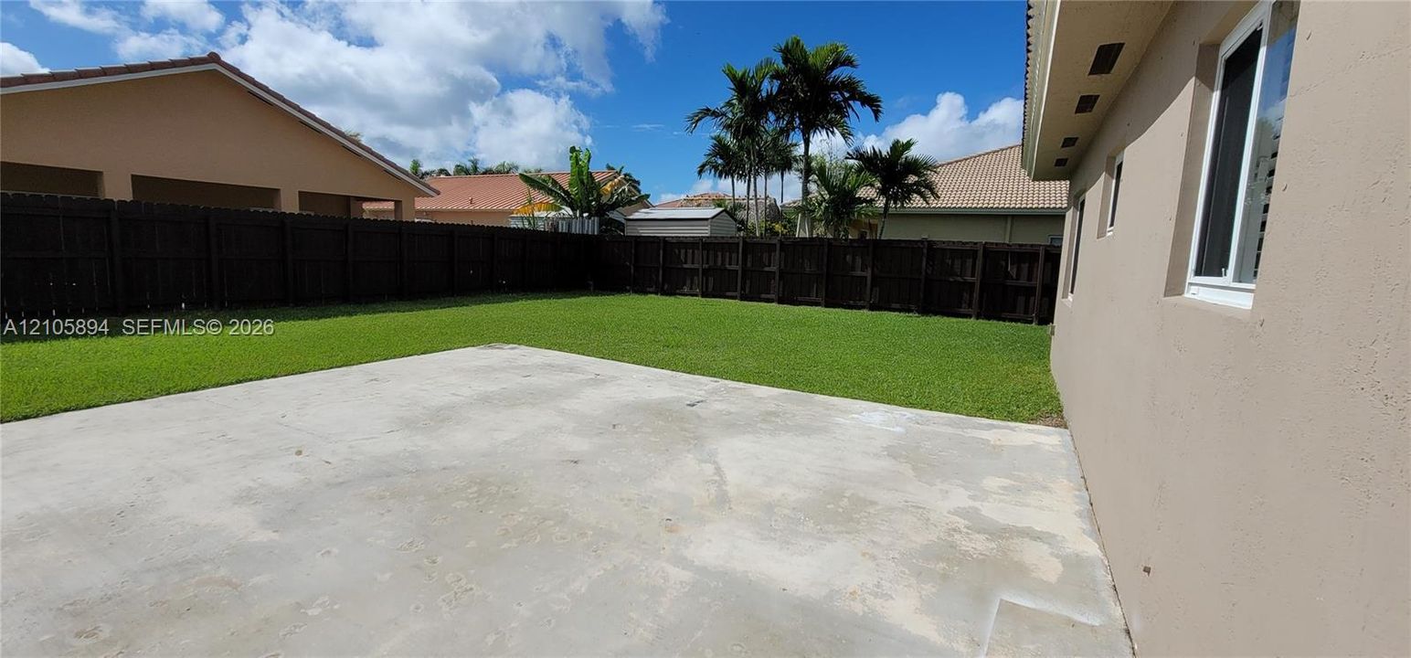 Backyard featuring a concrete patio, a level lawn, and perimeter wood fencing