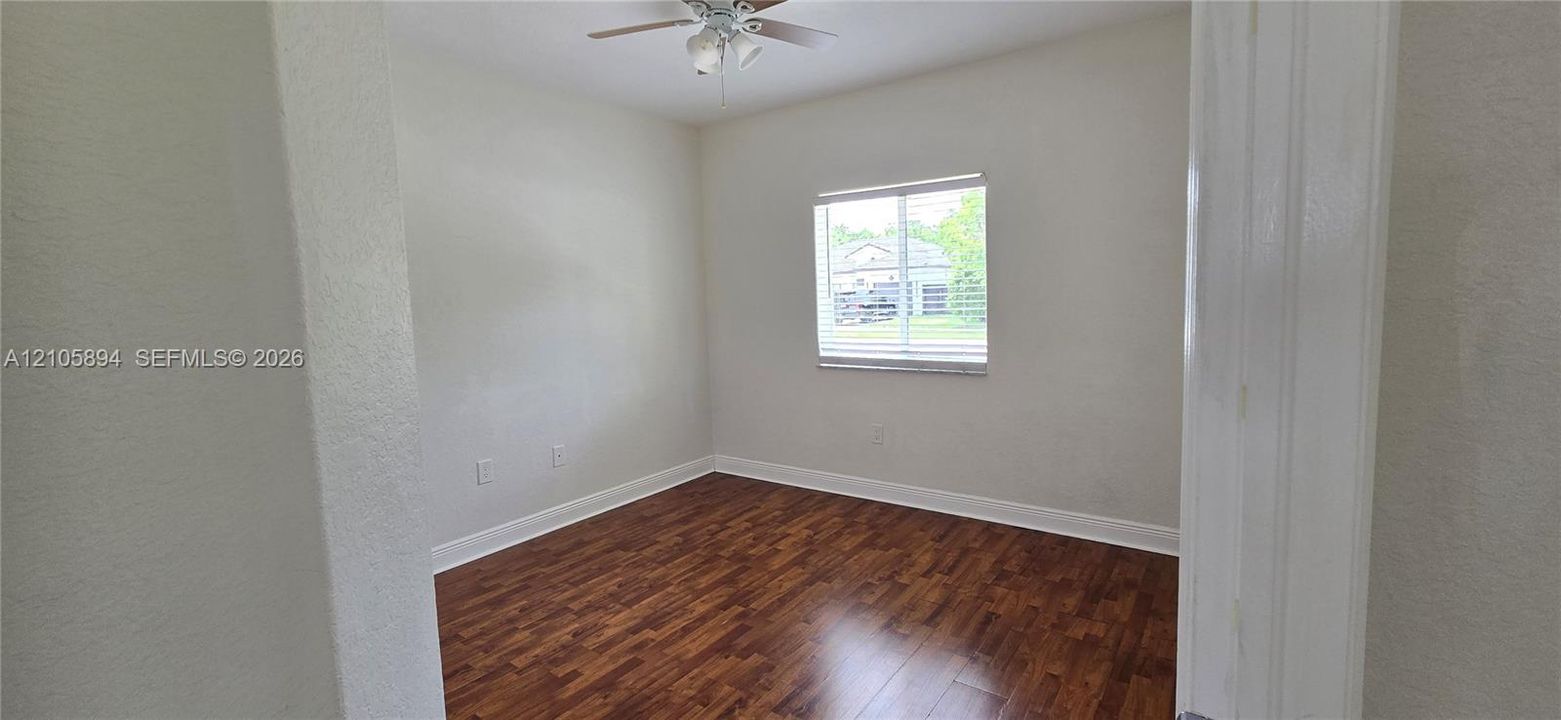 Room featuring wood-finish flooring, a neutral wall palette, a single-pane window, and a ceiling fan with integrated lighting