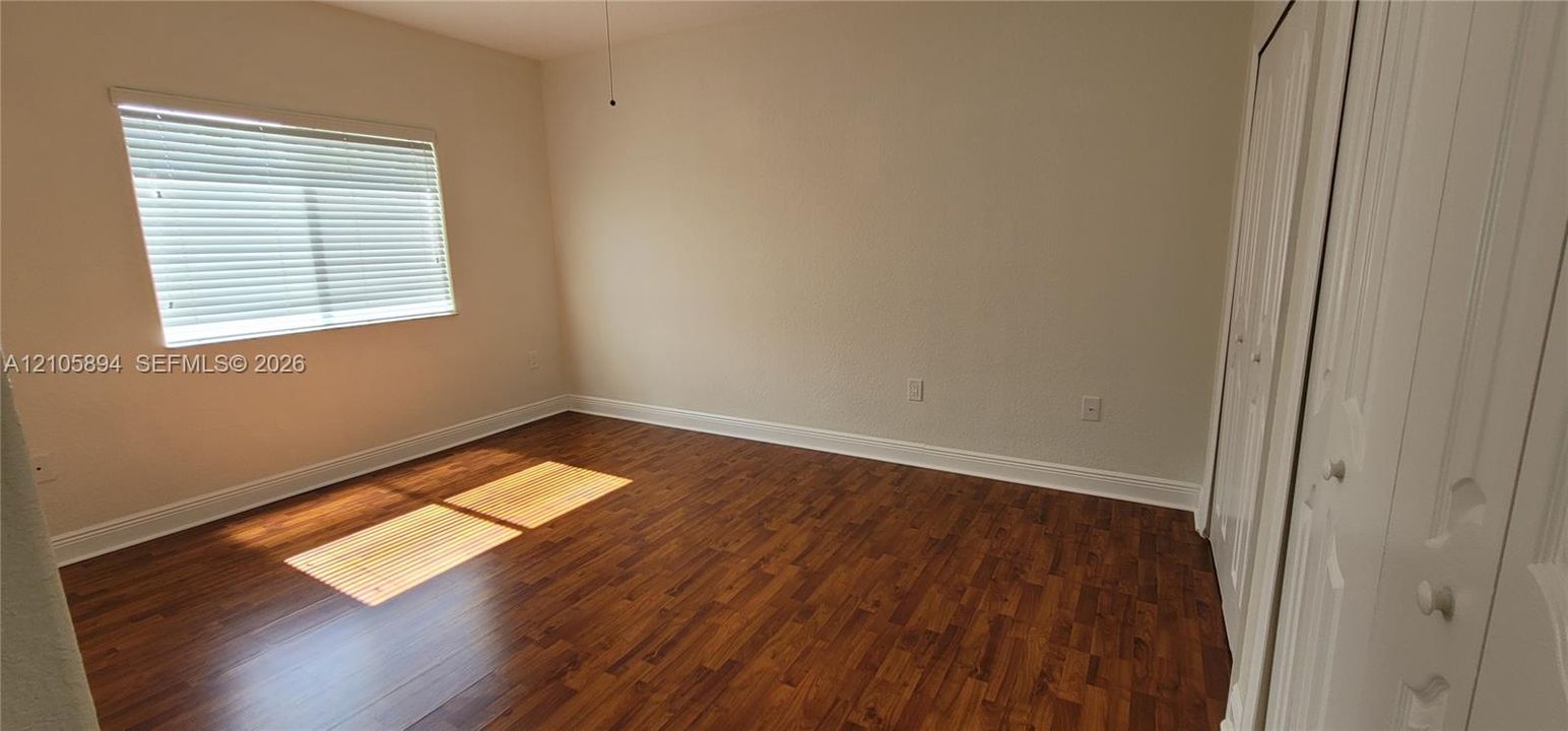 Room interior featuring wood-finish flooring, white walls, and built-in closet storage with paneled doors