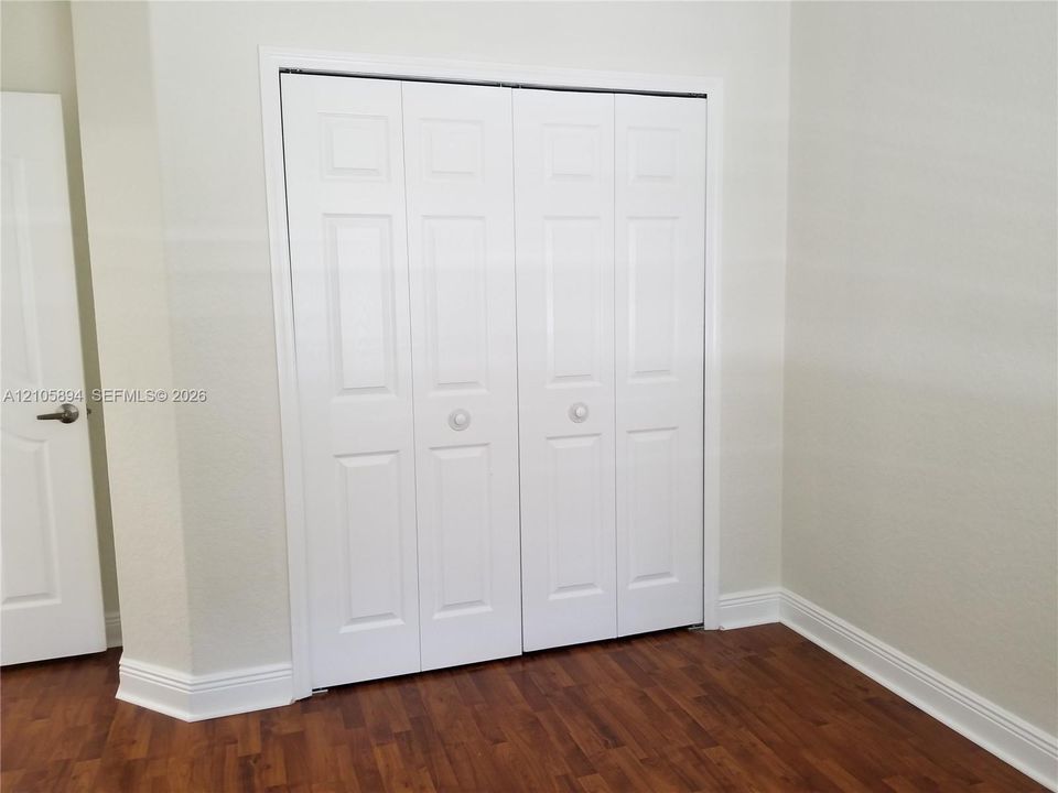 Wood-finish flooring paired with four-panel bifold closet doors and a coordinating interior swing door featuring a satin nickel lever handle