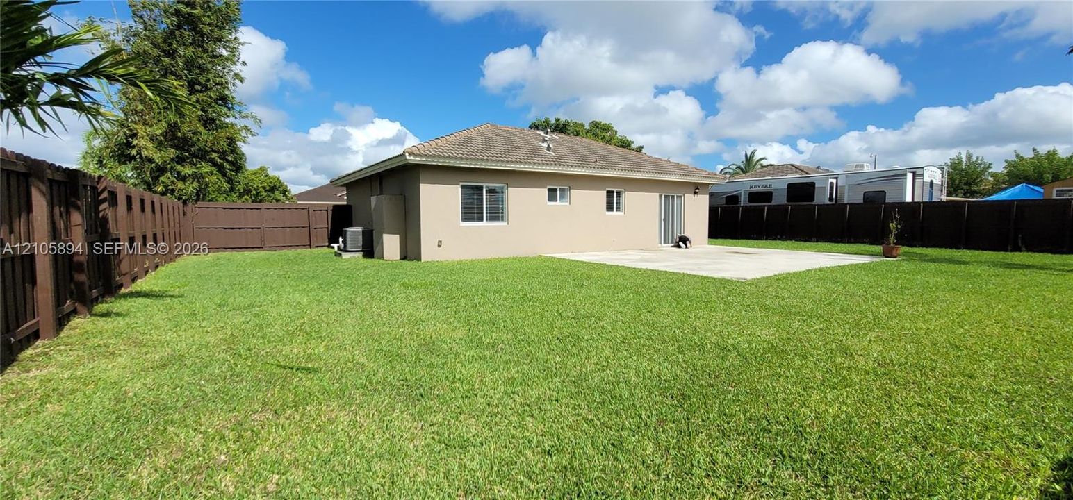 Expansive backyard featuring a level lawn, concrete patio, and full-perimeter wood privacy fencing