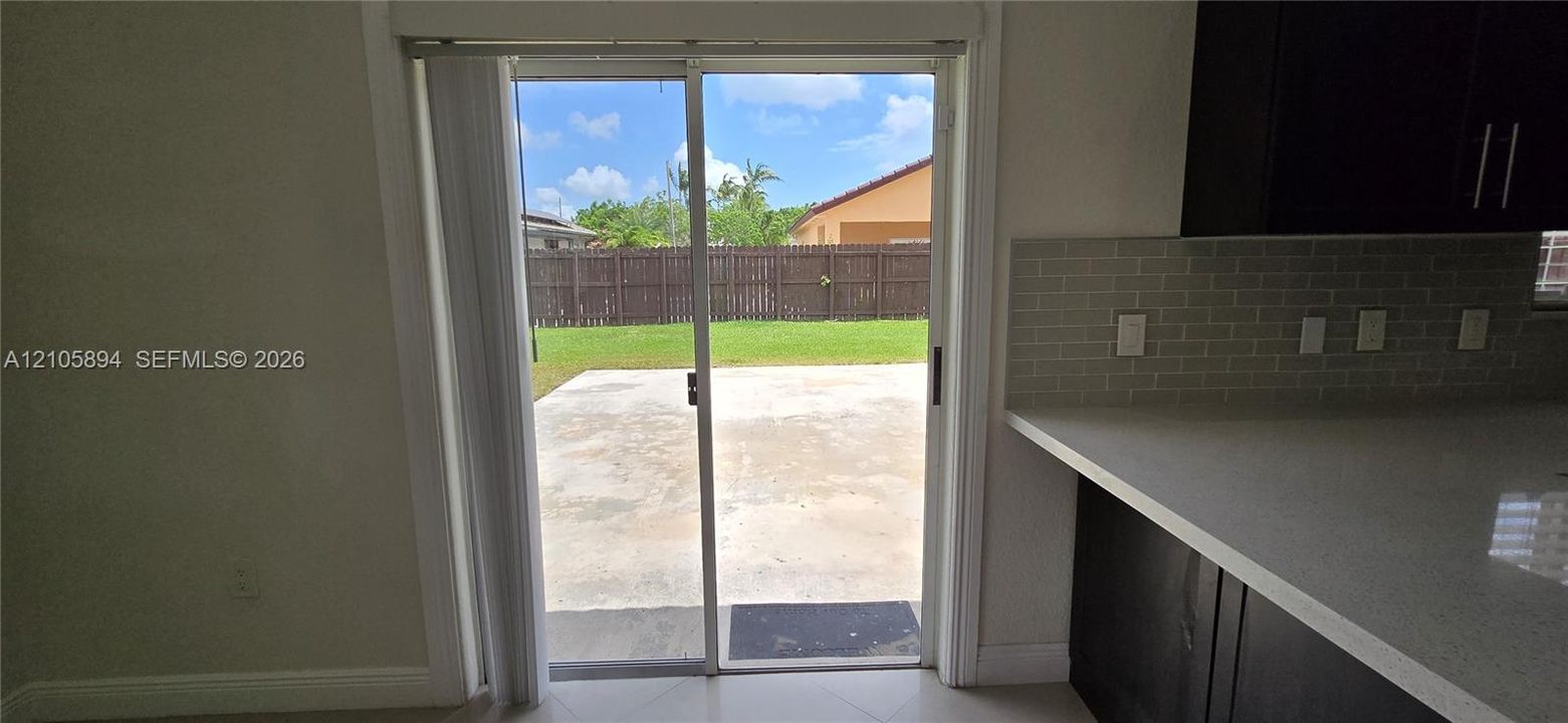 Sliding glass door featuring a light-toned countertop, subway tile backsplash, dark-finished cabinetry, and a concrete patio