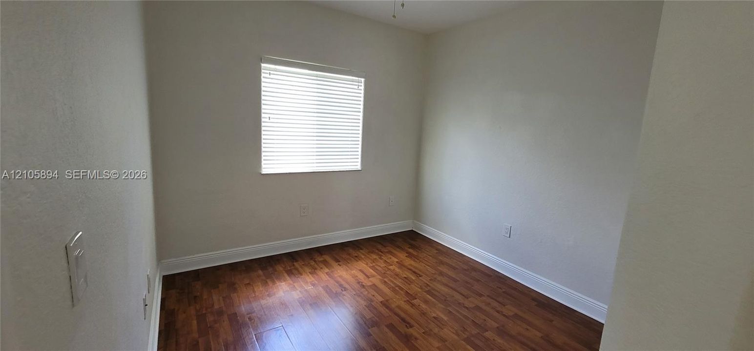 Interior room featuring wood-finish flooring, neutral wall tones, and a window fitted with horizontal blinds