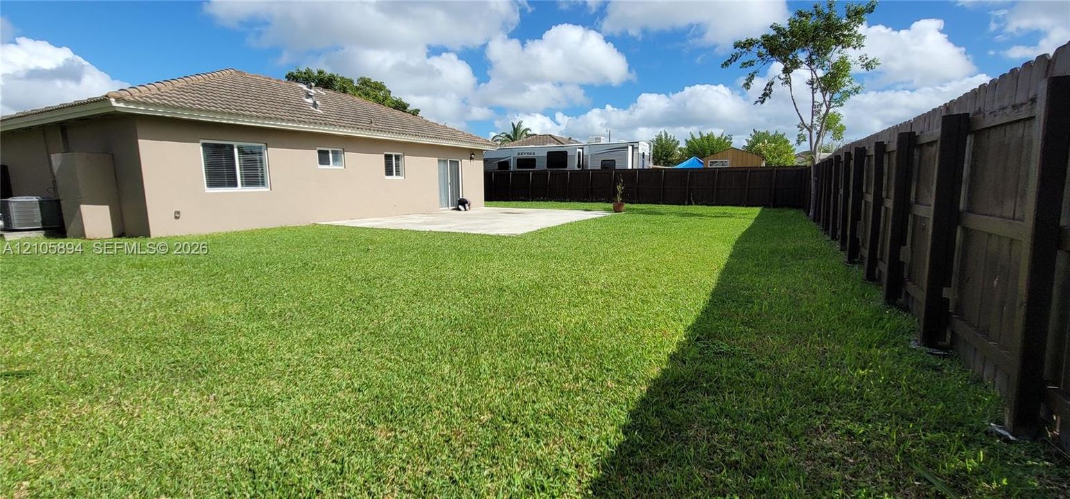 Rear exterior featuring a concrete patio, expansive grass lawn, and full-height wood privacy fencing