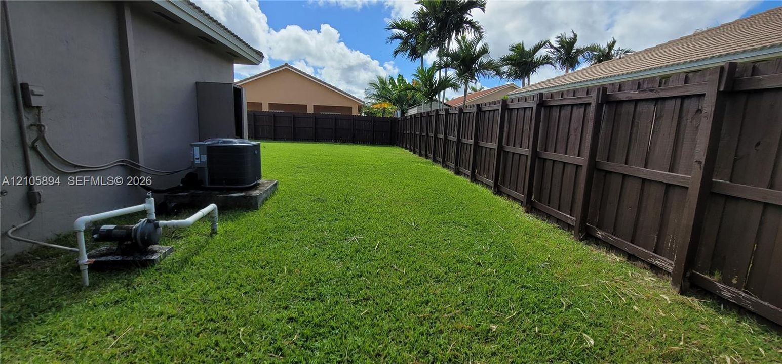 Fenced backyard featuring a manicured lawn, dark-stained wood privacy fencing, and exterior mechanical systems