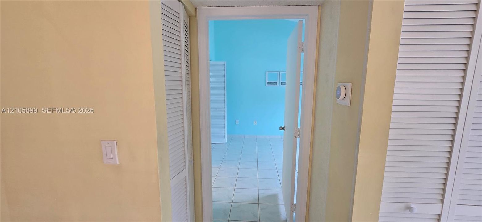 Interior doorway featuring white louvered closet doors, wall-mounted thermostat, and light-toned tile flooring