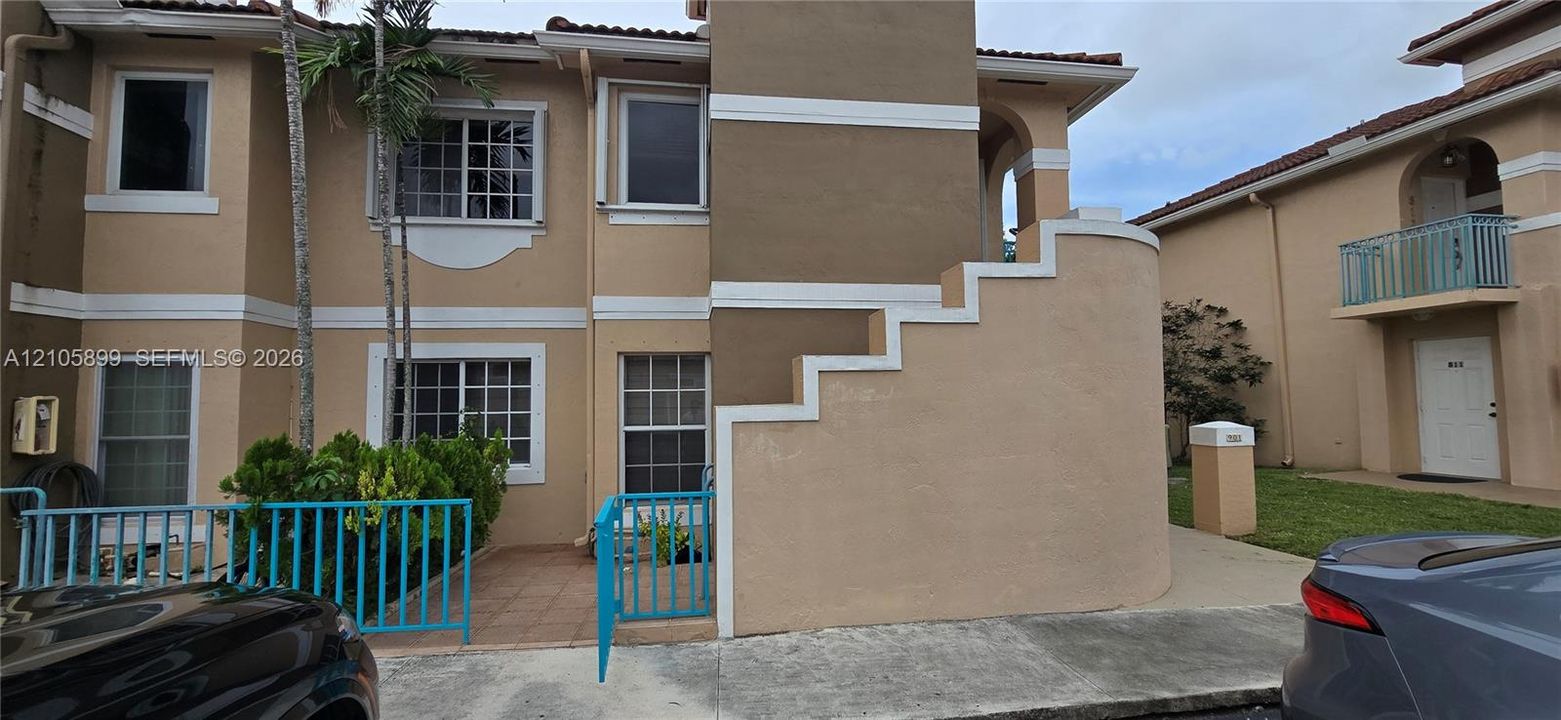 Multi-story exterior featuring a stucco facade with decorative trim, tile-accented patio, and a dedicated fenced entryway