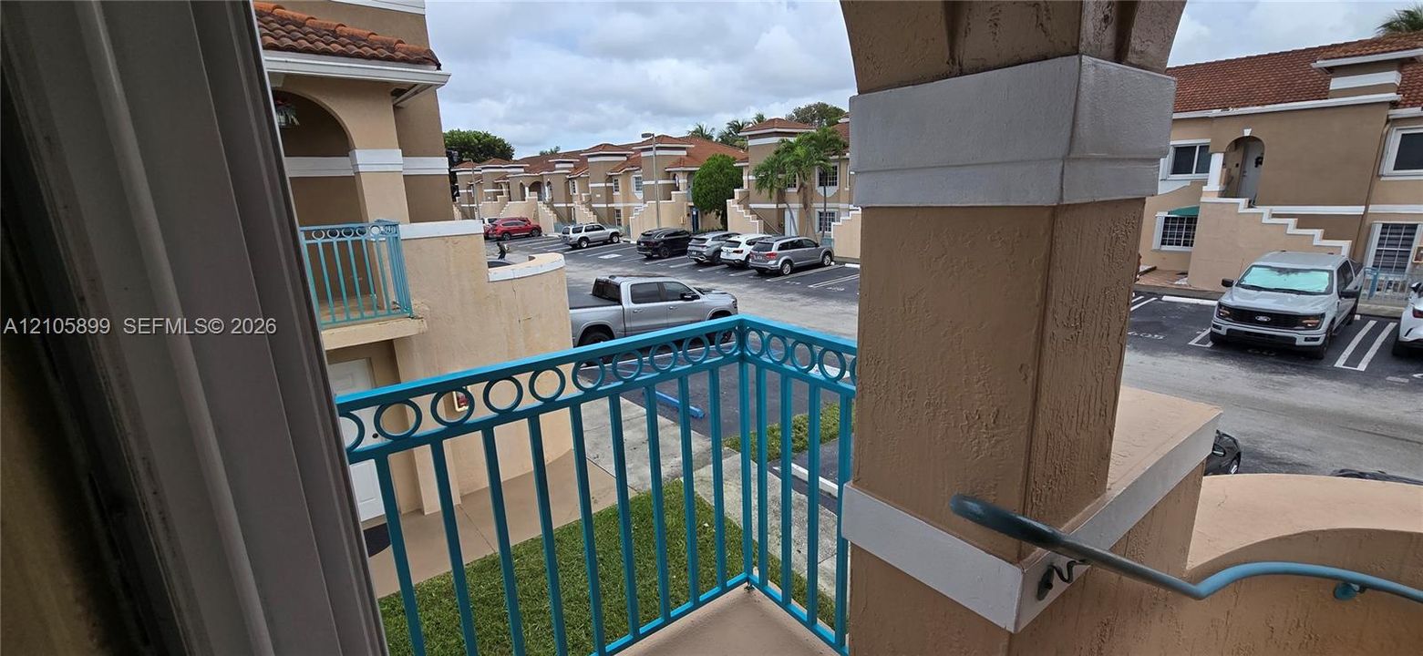 Balcony featuring blue metal railings, a stucco support pillar, and concrete flooring