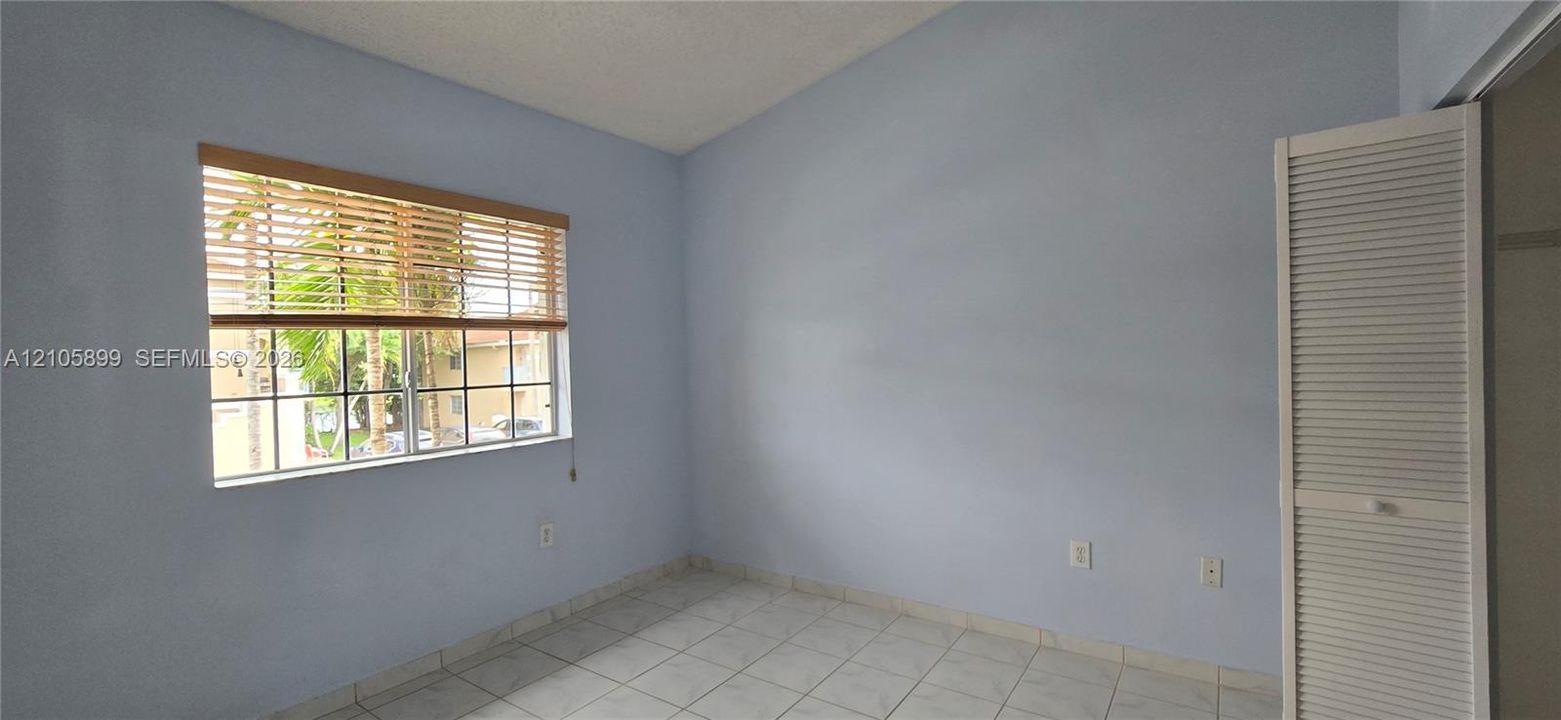 Room featuring neutral-toned ceramic tile flooring, a large window with slatted blinds, and a built-in louvered-panel closet door