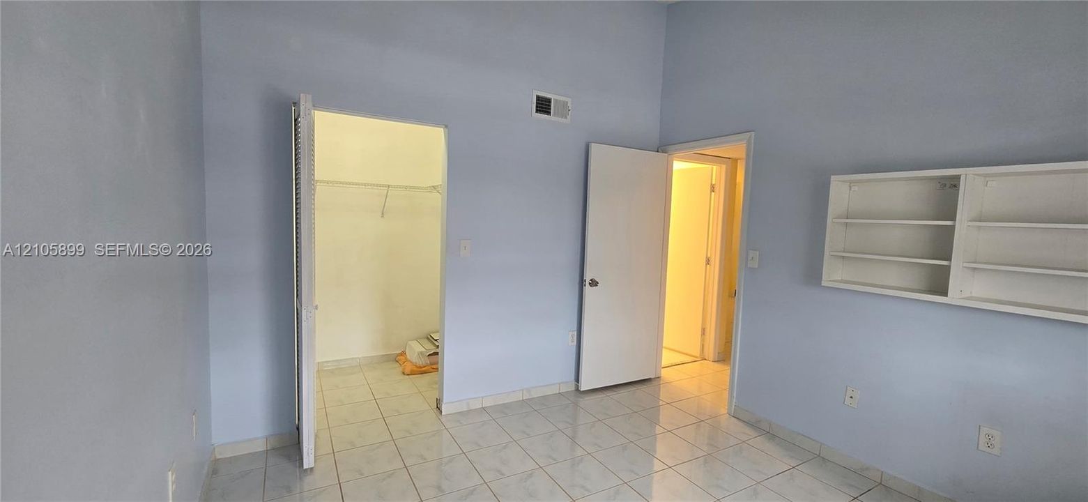 Room featuring light-colored tile flooring, built-in wall shelving, and a walk-in closet with integrated hanging rods