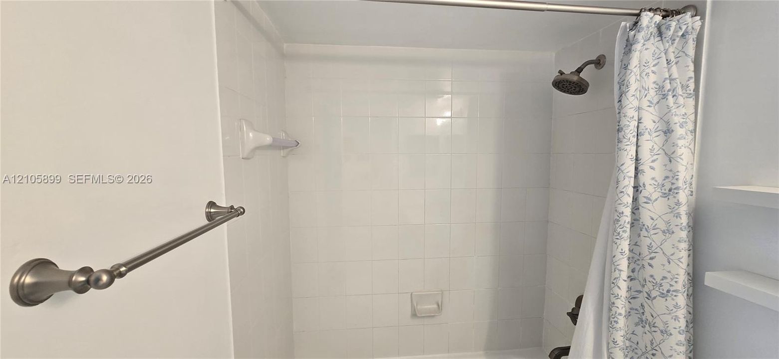 Shower-tub combination featuring white square wall tiles, built-in shelving, a brushed metal shower fixture, and a coordinated brushed metal towel bar