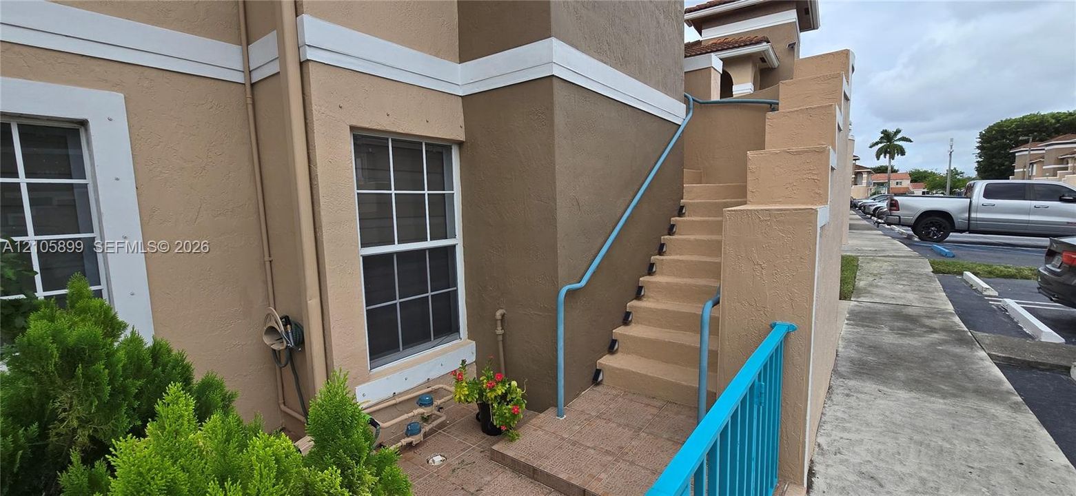Stucco exterior featuring multi-pane windows with white trim, concrete stairwell, and metal handrails