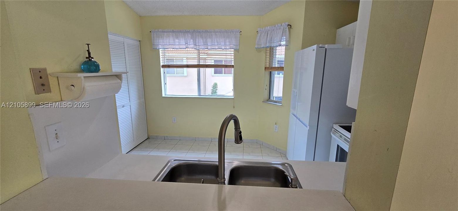 Kitchen area featuring a dual-basin stainless steel sink with a high-arch gooseneck faucet, tile flooring, white louvered closet doors, and windows with wood-slat blinds