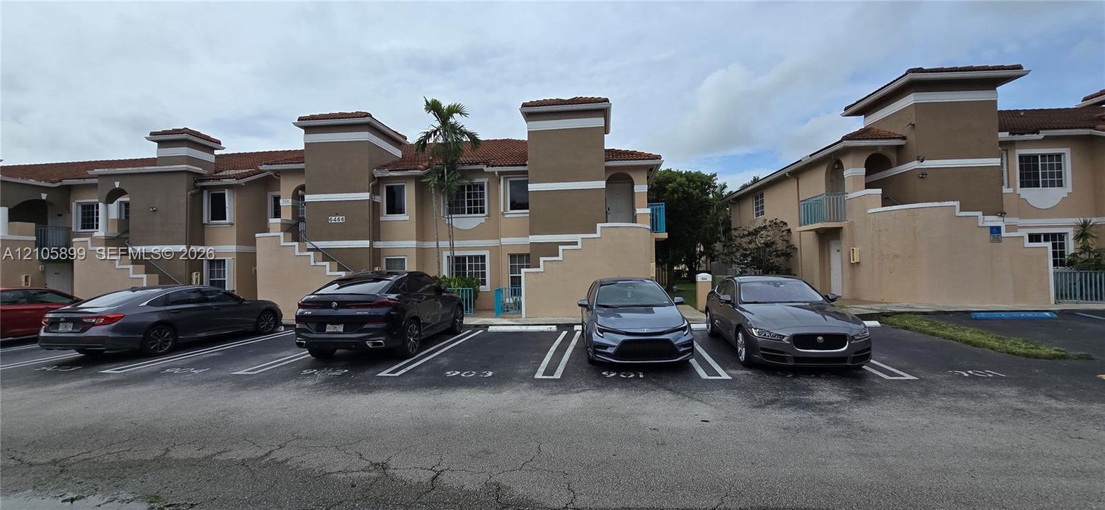 Multi-level exterior featuring stucco siding, tiled roofing, concrete stairs, and paved surface parking
