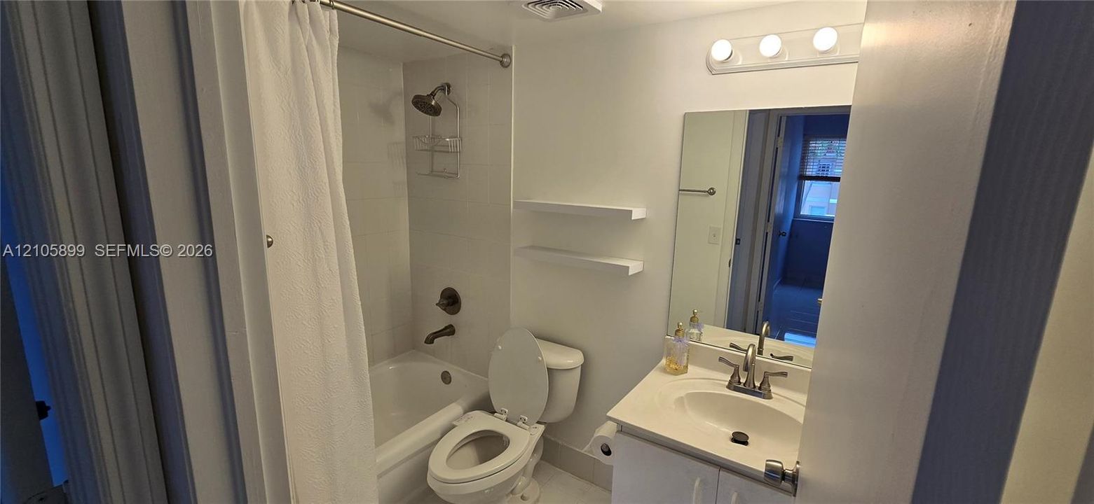 Bathroom featuring a vanity with a countertop basin, wall-mounted shelving, a full-width mirror, and a tub-shower combination with tile surround