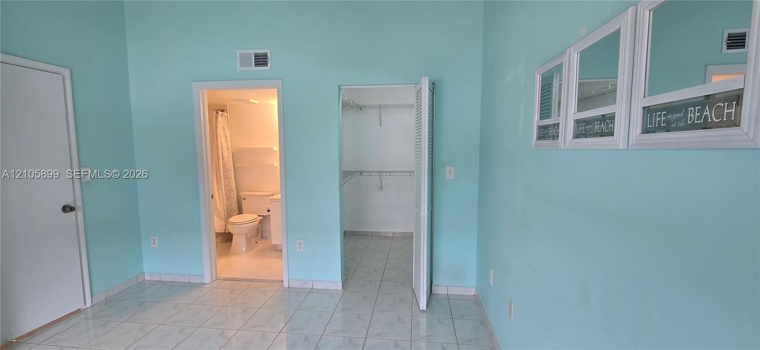 Room featuring ceramic tile flooring, a dedicated walk-in closet with integrated shelving, and an attached full bathroom
