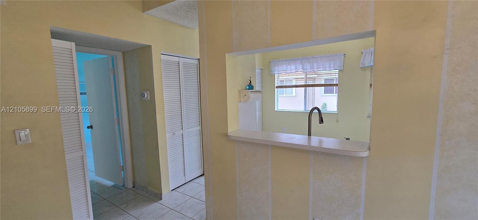 Pass-through window with a ledge, white louvered closet doors, and tile flooring