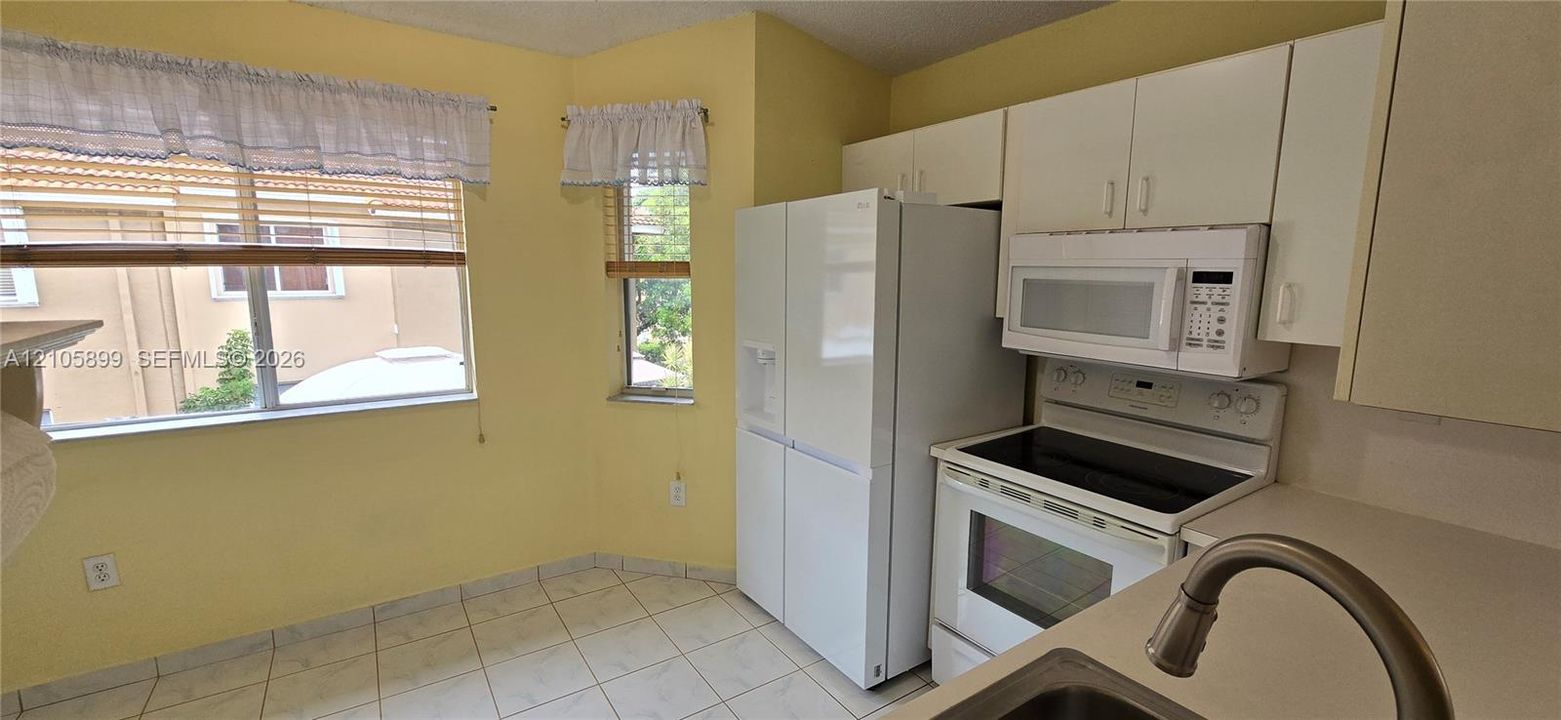 Kitchen featuring white cabinetry, tile flooring, built-in microwave, integrated refrigerator, and stainless steel sink with a high-arch faucet