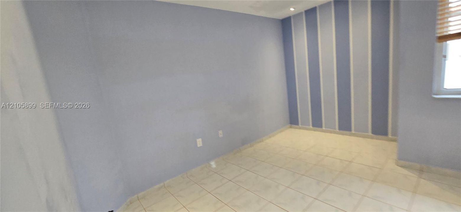 Room featuring light-toned tile flooring, recessed ceiling lighting, and a vertical stripe accent wall