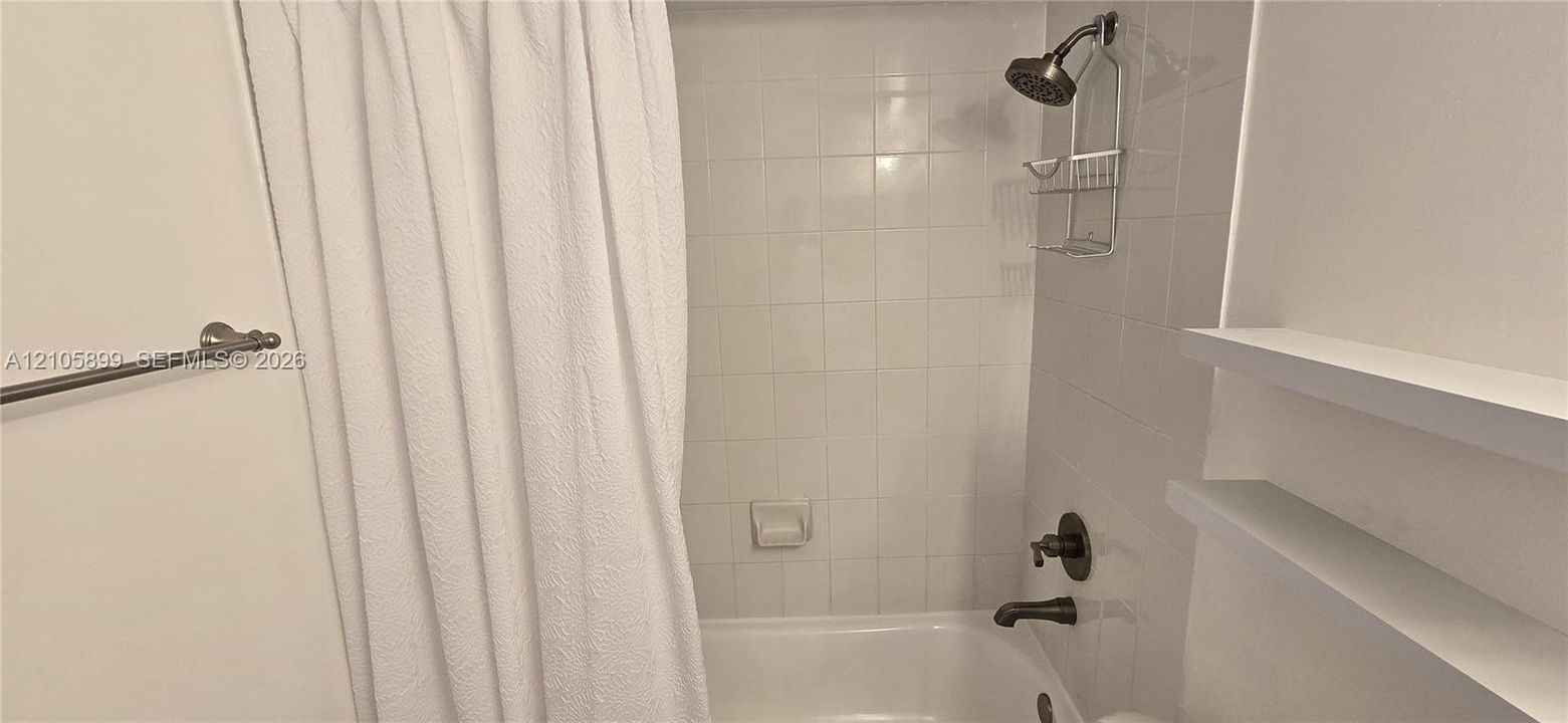 Bathtub surround featuring white square ceramic wall tiling, oil-rubbed bronze plumbing fixtures, and dual integrated floating shelves