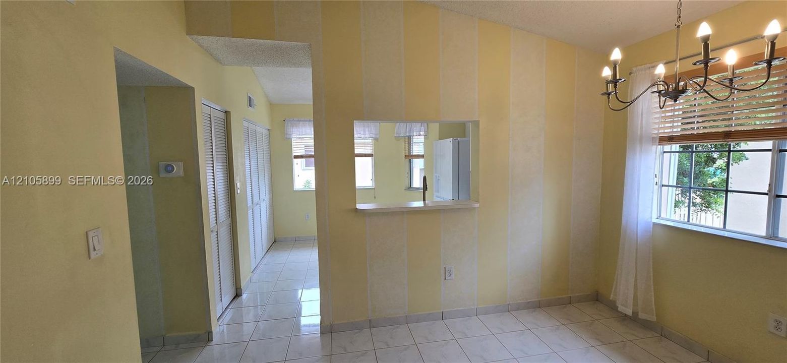 Dining area featuring ceramic tile flooring, a multi-arm chandelier, louvered closet doors, and a pass-through opening