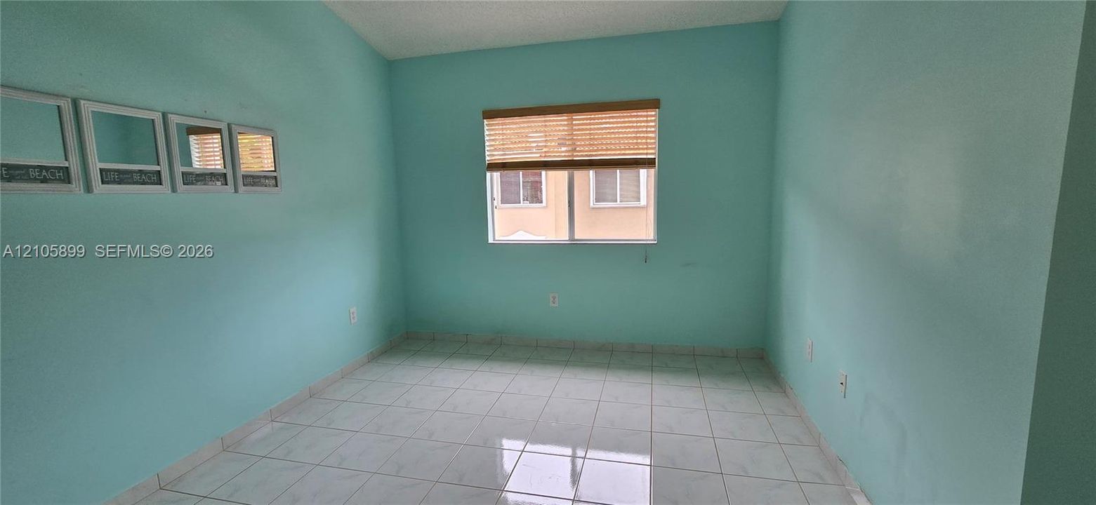 Interior room featuring white tile flooring, painted walls, and a window with a woven wood-finish blind