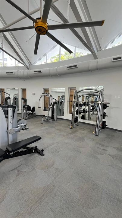 Vaulted ceiling with oversized industrial ceiling fan, clerestory windows, wall-to-wall mirrors, and resilient commercial-grade flooring