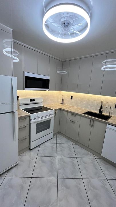 Kitchen featuring high-gloss cabinetry, stone-patterned countertops, a subway tile backsplash with under-cabinet lighting, a built-in microwave, and a flush-mount circular ceiling fixture