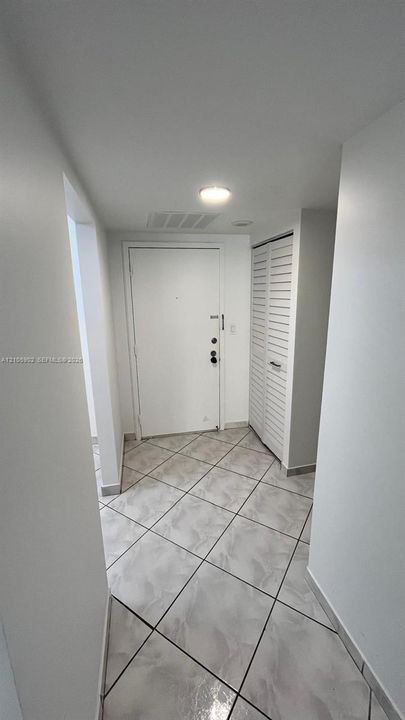 Entryway featuring large-format ceramic tile flooring, a white metal entry door with a deadbolt, and a built-in closet with louvered bi-fold doors
