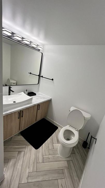 Bathroom featuring wood-finish cabinetry, stone-patterned vanity countertop with a vessel sink, matte black hardware, and herringbone-patterned flooring