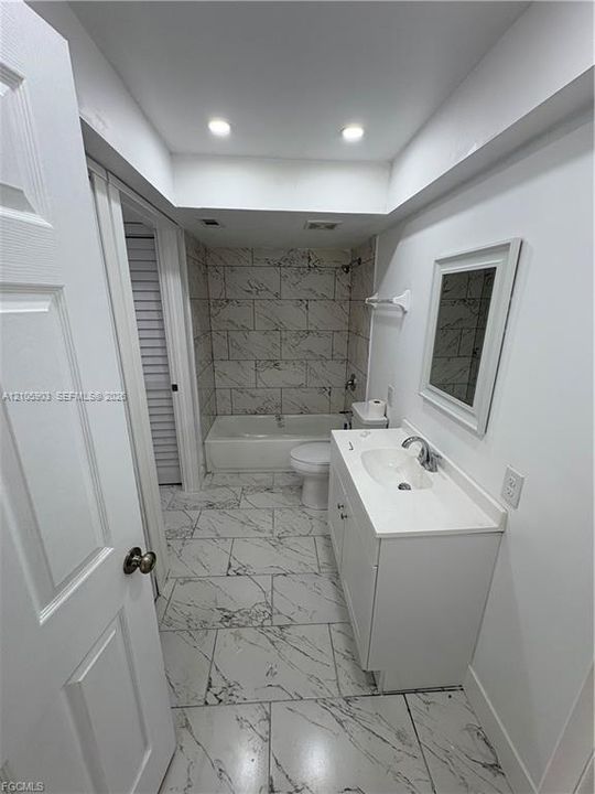 Bathroom featuring large-format tile flooring, a white vanity with an integrated basin, a framed wall mirror, and a tub-shower combination with floor-to-ceiling tile surround