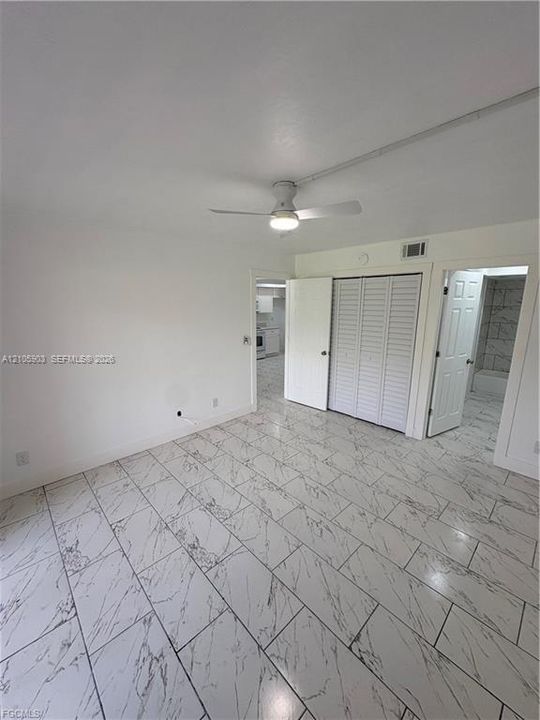 Neutral-toned interior featuring large-format stone-patterned tile flooring, louvered bi-fold closet doors, and a ceiling-mounted light fixture with integrated fan