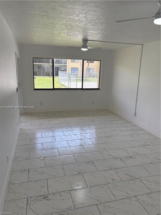 Interior space featuring large-format tile flooring with a neutral veined pattern, a wide picture window, and dual ceiling fans