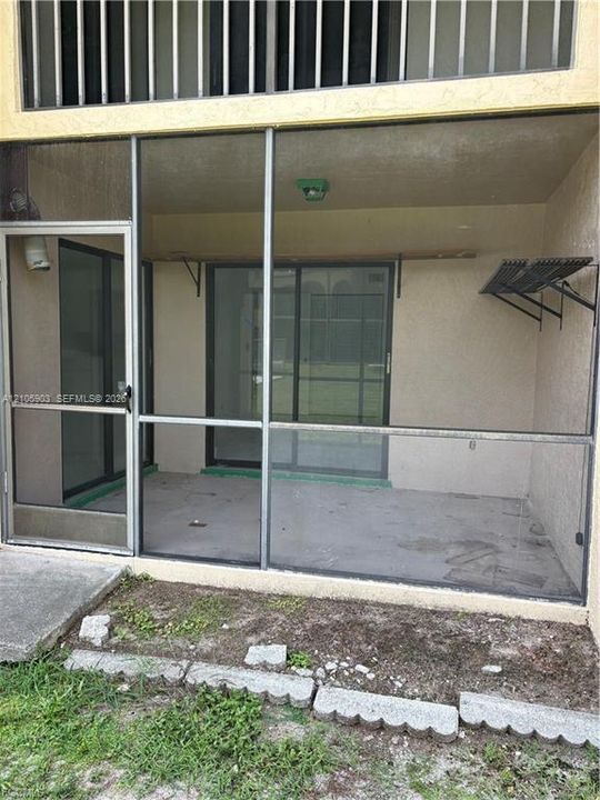 Screen-enclosed patio featuring a concrete floor, aluminum-framed door, sliding glass entry, and attached wall-mounted shelving